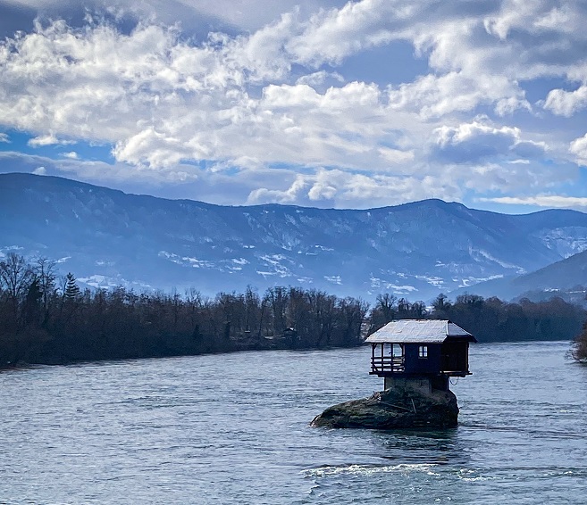 white and black house on body of water near green trees under white clouds and blue in Serbia, Photo by Nikola Aleksic on Unsplash